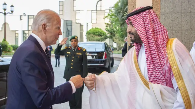 US President Joe Biden (wearing a blue suit over a white shirt) fist bumps Saudi Crown Prince Mohammned bin Salman who is wearing traditional Saudi clothing.