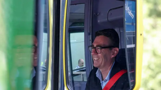 Burnham smiles sitting in a bus with the picture taken of his reflection in the wing mirror