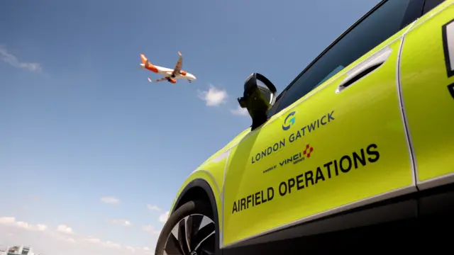A yellow car with the words 'Airfield Operations' printed on the side. A white and orange plane flies overhead.