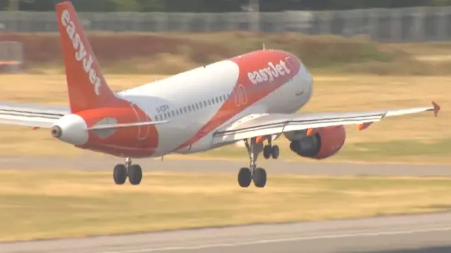 An orange and white EasyJet plane landing on a runway.