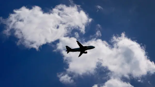 A shadow of a passenger plane against a blue and cloudy sky.