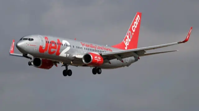 A plane with silver and red Jet2 livery, in the air with landing gear deployed.