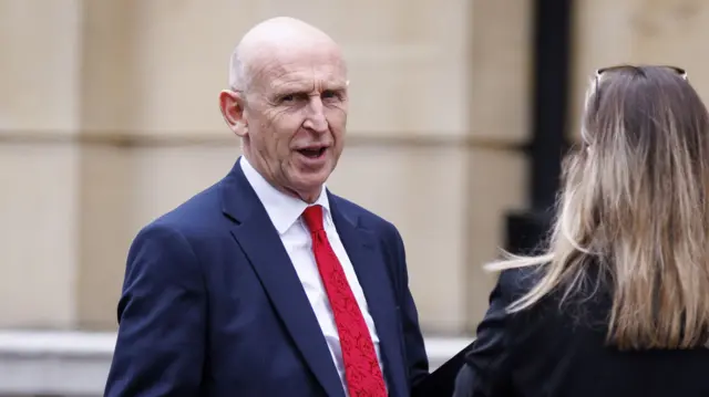 John Healey wears a navy suit and a red tie