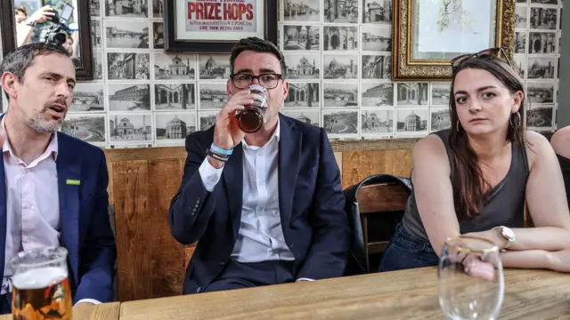Andy Burnham drinks a pint in between a man and a woman