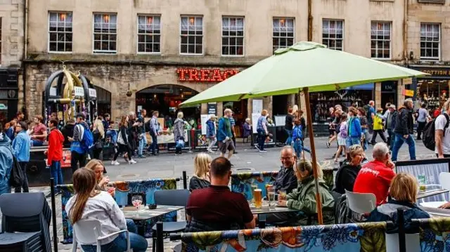 A busy street in Edinburgh with people drinking beers and eating food outside restaurants