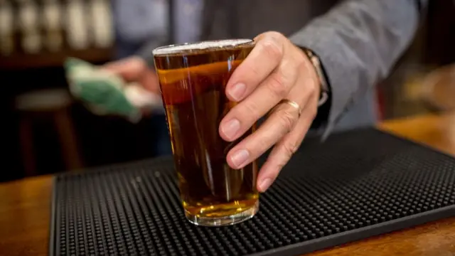 A pint of beer on a counter being reached for by a man with a wedding ring on his finger.