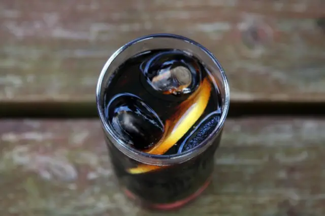 A glass of coca cola with a slice of lemon in it