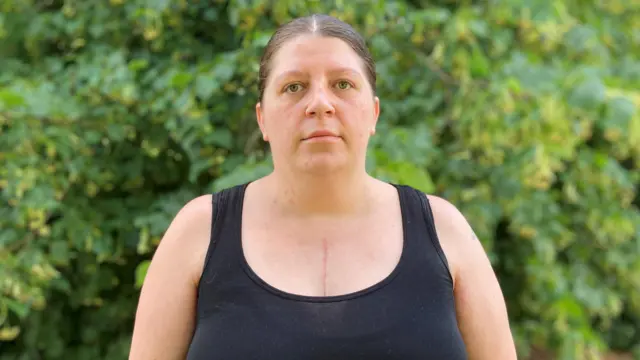 A woman in a black top with her hair tied back looks at the camera.