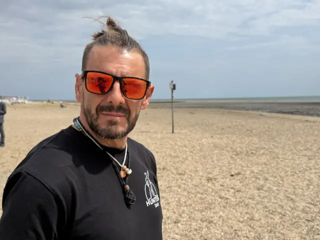 A man who is wearing sunglasses and a black top while on the beach