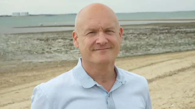 A man wearing a blue shirt standing on the beach