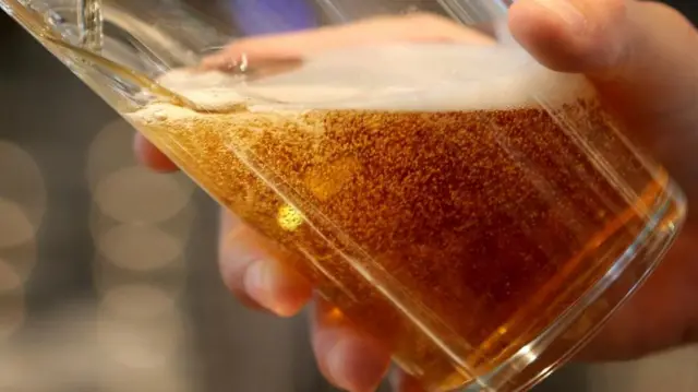 A close up picture of a hand holding a pint glass while beer is being poured into it