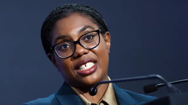 Kemi Badenoch, a woman, wearing a blue blazer speaking into a microphone.