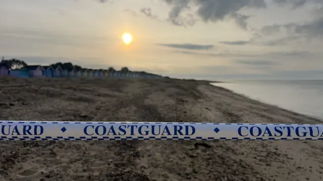 Coastguard tape across an area of beach, Beach huts are visible in the background.