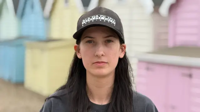 A woman wearing a sun hat and standing in front of a beach hut