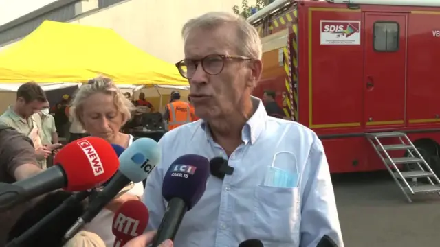 The Mayor of Lège-Cap Ferret Philippe de Gonneville puts as he speaks to reporters. He is wearing a blue shirt and has a mask in his shirt's pocket