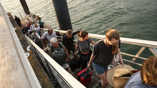 People walking up a ramp by the sea carrying bags