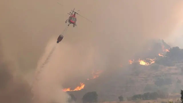 A helicopter dropping a bucket of water over a huge hillside fire