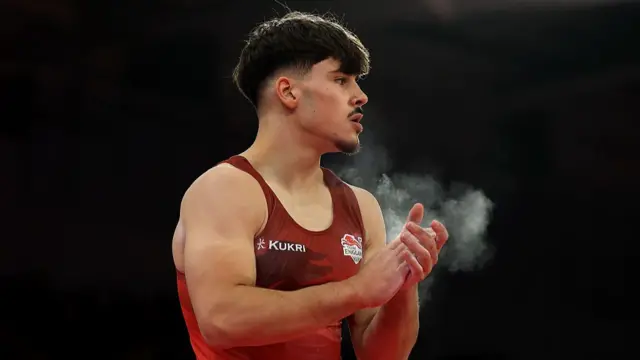 Gabriel Langton claps his hands covered with chalk dust while wearing a red England vest