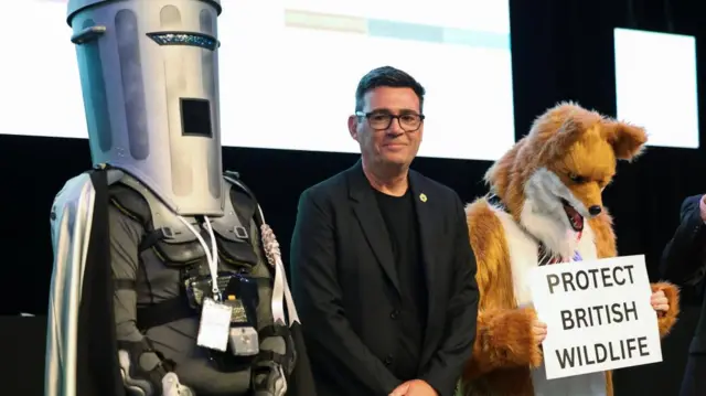 Andy Burnham at the result of the Makerfield by-election in June, stood beside Count Binface and an individual dressed as a furry fox.