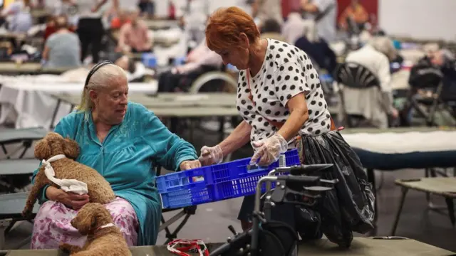 An evacuee sits with two dogs at the Bordeaux-Lac Exhibition Centre, which has been turned into a shelter for people displaced by a wildfire burning nearby