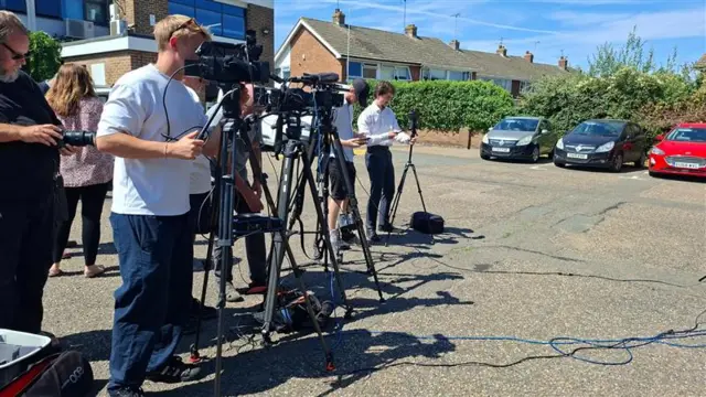 Cameras on tripods and peole with cameras and notebooks are gathered.