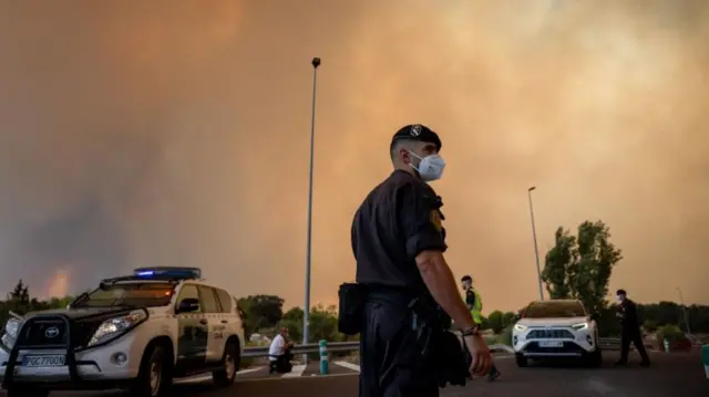 A Civil Guard officer wears a protective mask as smoke from a wildfire obscures the sky in Cenicientos
