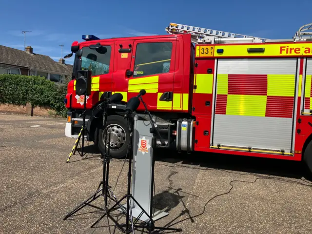 A fire engind with a stand inf ront of it with micorphones.