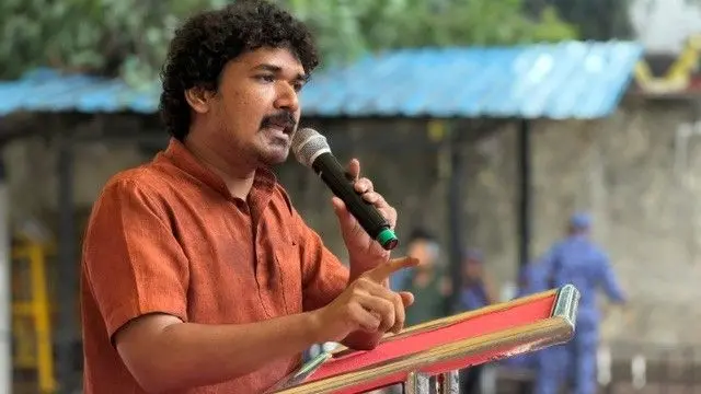 Viraaj Devang in a rust brown shirt speaking at a podium