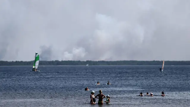 People enjoy the beach in Lacanau as a wildfire burns in a forest area near the Bassin d'Arcachon in the Gironde department amid worsening drought conditions following a heatwave and water shortages across much of France, July 23, 2026