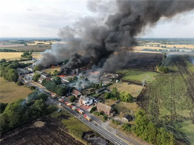 Thick black smoke plumes fill the air. Orange flames can be seen below.