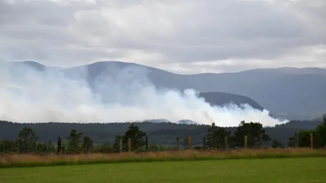 Smoke rising above hills across a field covering the sky line
