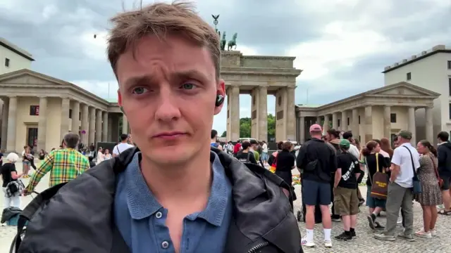 Dressed in a black raincoat and blue polo, Der Spiegel correspondent Timo Lehmman reports from Berlin
