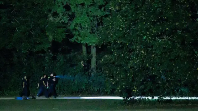 Police search the Tiergarten park at night with a torch.