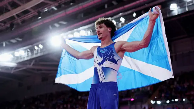 Reuben Ward draped in a Scotland flag after winning men's all-around gold