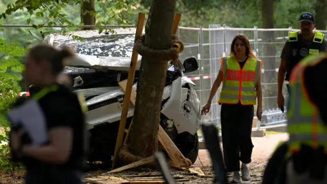 A police officer walks past the crumpled front of a white vehicle
