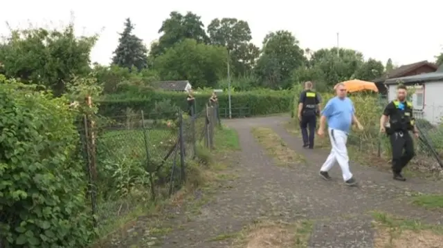 People walk along a path by green gardens