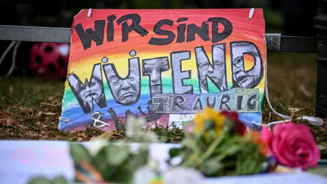 A colourful sign shows the faces of politicians including Donald Trump and Friedrich Merz in the word 'Wutend'