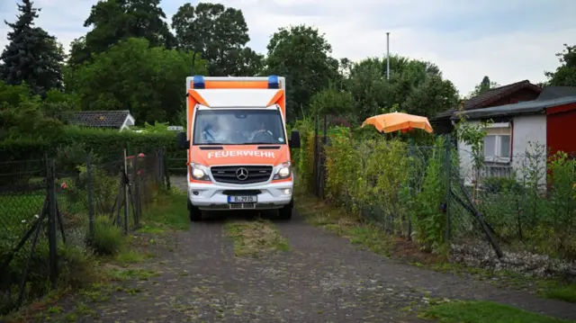 An ambulance parked on a dirt path by gardens