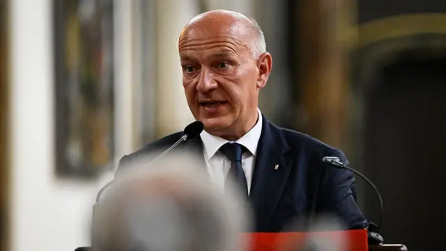 Kai Wegner is shown speaking behind a lectern, wearing a suit and tie.