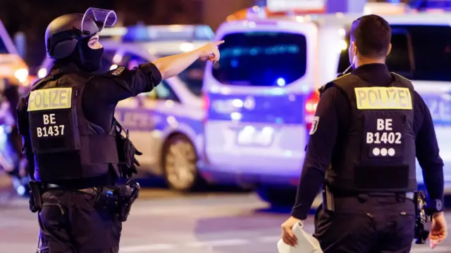 A police officer carrying a machine gun (L) and a colleague talk near the scene where several people were injured on the sideline of the Christopher Street Day (CSD) parade in Berlin