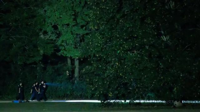 Several police officers are seen walking near some trees in Tiergarten park
