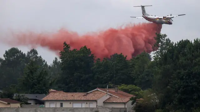 A plane flying over a house and trees dropping fire retardant in south west France