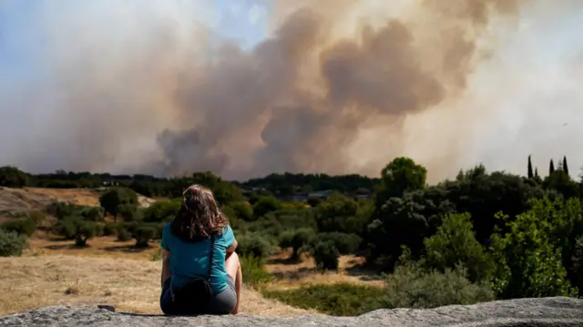 A woman looks as smoke rises from a wildfire in San Martin de Valdeiglesias, in the Madrid region, on Sunday