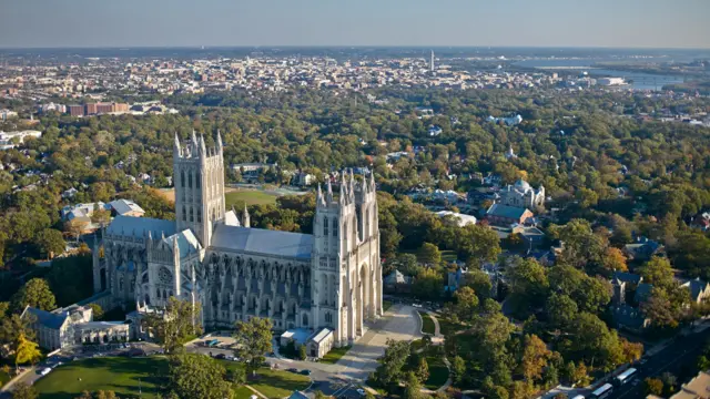 aerial image of gothic cathedral amid trees with city and river in background