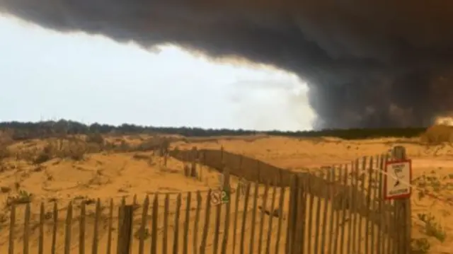 A foggy beach with a smoke cloud in the distance