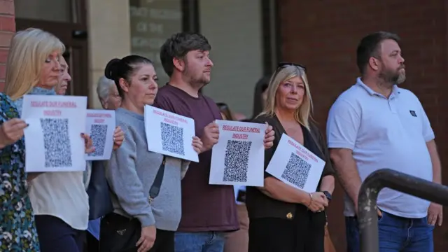 People demonstrate outside Hull Crown Court, Kingston-upon-Hull, ahead of the sentencing of funeral director Robert Bush. They are holding pieces of paper with a QR code and text saying "Regulate our funeral industry".