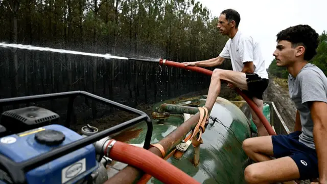 Farmers spray water on hotspots to help firefighters battle the wildfire in Saint-Jean-d'Illac, west of Bordeaux, on July 27, 2026, during wildfires in the Gironde region, southwestern France.
