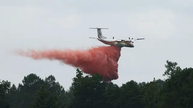 A plane flying over trees dropping fire retardant in south west France