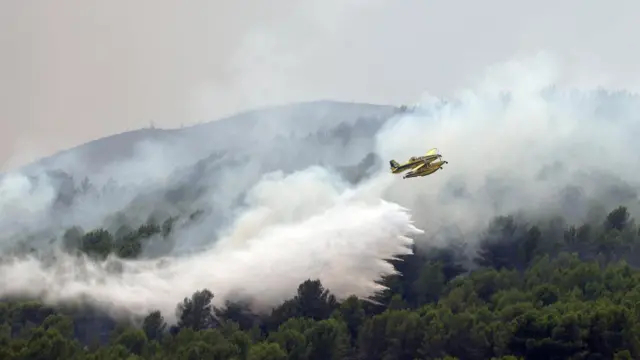 A firefighting plane makes a drop during a wildfire in Onda, Spain. A large trail of water can be seen behind the aircraft