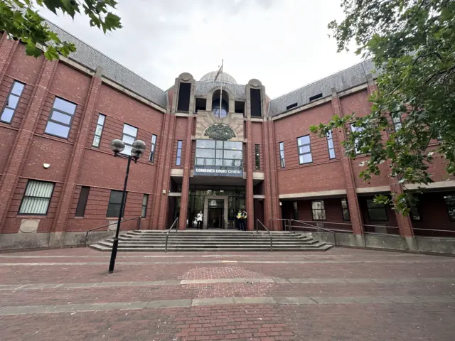 An exterior shot of Hull Crown Court - two police officers are standing on the top steps by the front door. it's a large red brick building.